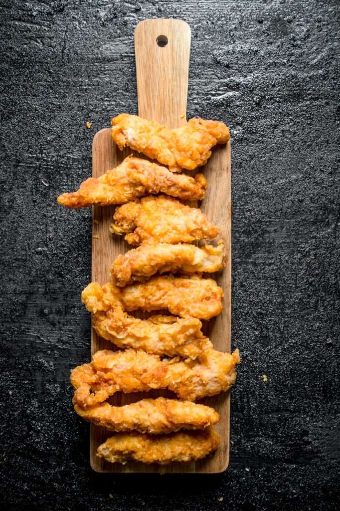 Chicken strips on a wooden cutting Board.